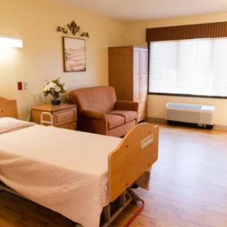 A clean and well-lit hospital room with a single bed, a comfortable chair, and a large window.