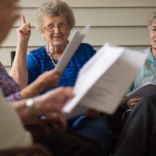 A group of elderly individuals engaged in reading and discussion.
