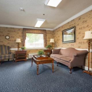 A cozy living room with traditional furniture, featuring a sofa, armchair, and wooden table set against patterned wallpaper.