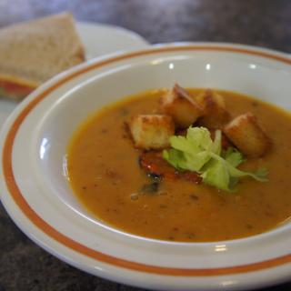 A bowl of soup garnished with croutons and celery, accompanied by a slice of bread.