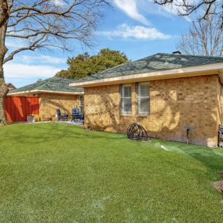 A view of a brick residential house with a grassy backyard and trees.