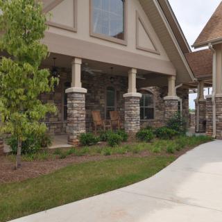 A house with a covered porch featuring stone columns and a neatly landscaped lawn.