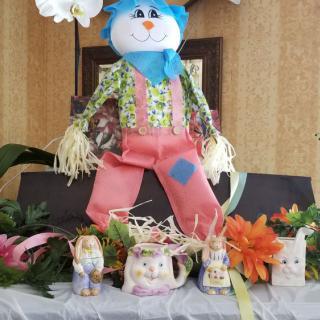 A festive table display featuring a handmade scarecrow, surrounded by ceramic animal figures and colorful flowers.