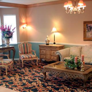 A traditionally decorated living room featuring a floral carpet, elegant armchairs, and a chandelier.