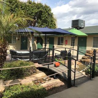 A small outdoor patio with a bridge over a garden area, surrounded by trees and shaded by umbrellas.