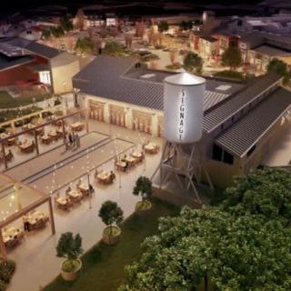 Aerial view of a lively industrial-style outdoor dining area at night, featuring a prominent water tower.
