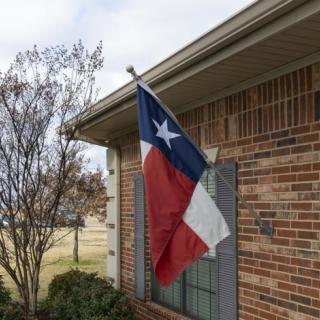 A Texas flag is mounted on a brick house under a cloudy sky.