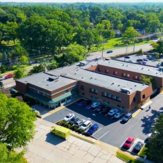 An aerial view of a brick office building surrounded by trees with a parking lot in the foreground.