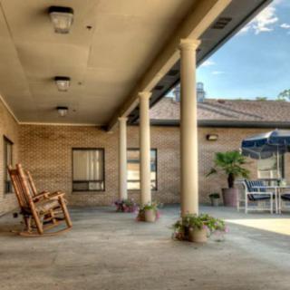 A spacious outdoor patio with columns, featuring a rocking chair and tables under umbrellas.