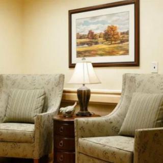 A cozy living room setup featuring two armchairs, a side table with a lamp, and a landscape painting on the wall.