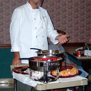 A chef presenting dishes at a buffet setup.
