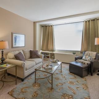 A cozy living room with a sofa, armchair, and coffee table, tastefully decorated with lamps and a rug.