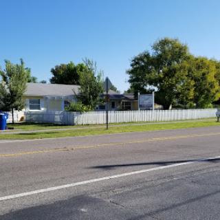 A peaceful suburban home with a white fence and trees under a clear blue sky.