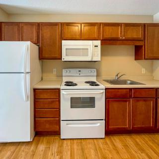 A modern kitchen with wooden cabinets, featuring a refrigerator, oven, microwave, and sink.