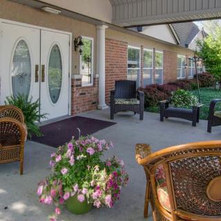 A cozy porch with wicker chairs, potted flowers, and a building entrance.