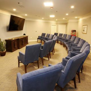 A meeting room with blue chairs arranged in a curved formation facing a large television.