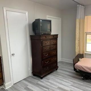 A bedroom featuring a vintage television on top of a wooden dresser with modern flooring.