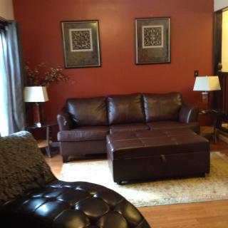 A cozy living room with a brown leather sofa and matching ottoman, accented by two floor lamps and wall art.