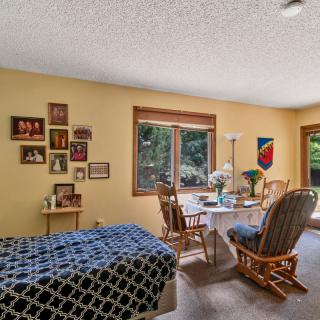 A cozy bedroom with a bed, table, and chairs set against a window with decorative wall pictures.