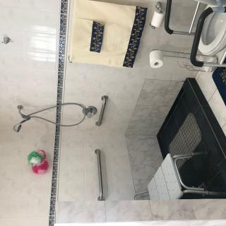 A bathroom with a shower, glass door, and various fixtures such as grab bars and a towel rack.