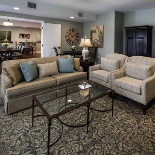 A cozy living room with a sofa, two armchairs, and a glass coffee table on a patterned rug.