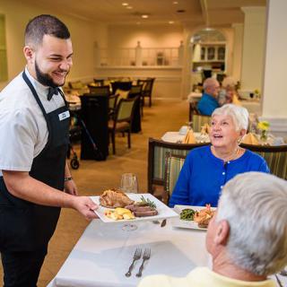 A waiter serves food to an elderly couple in a restaurant.