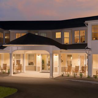 A well-lit building with a porch and rocking chairs at dusk.