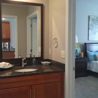 A view from a bathroom into a bedroom, featuring a sink with a mirror and adjacent sleeping area.