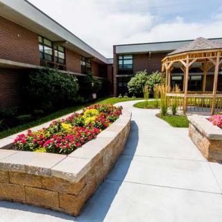 A beautifully landscaped outdoor garden area with colorful flowers, a gazebo, and a brick building in the background.