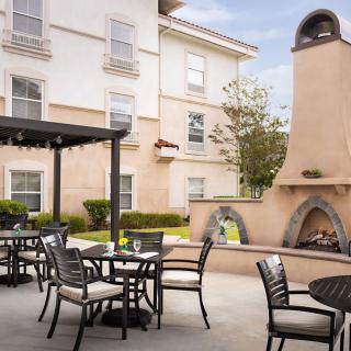 A cozy outdoor patio area with tables, chairs, and a fireplace next to a building.
