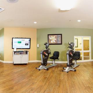 A well-lit exercise room featuring stationary bikes and a large screen.