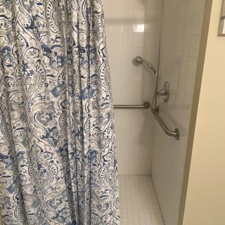 A bathroom shower with a floral-patterned curtain and safety grab bars.