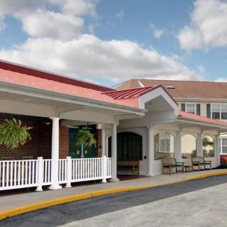 The image shows the exterior of a building with a prominent entrance and red roof under a partly cloudy sky.