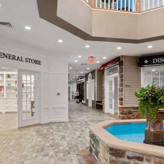 A modern indoor shopping area with various storefronts and a central fountain.
