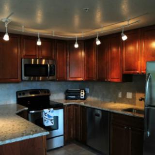 A modern kitchen featuring wood cabinets, granite countertops, and stainless steel appliances illuminated by track lighting.