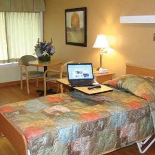A cozy bedroom with a laptop on a bed, featuring a table, lamp, and floral decor.