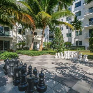 A tranquil garden space with a giant chess set in the courtyard of an apartment building, surrounded by lush palm trees.