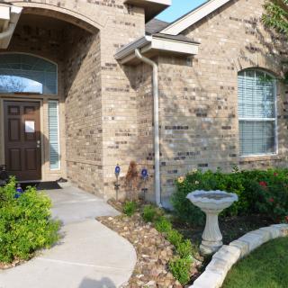 A brick house with a landscaped front yard featuring a walkway and birdbath.
