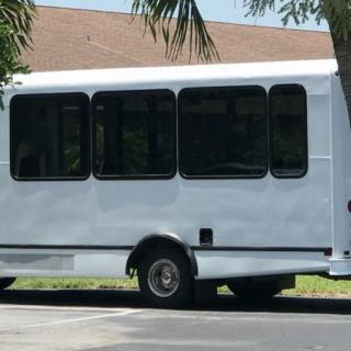 A white shuttle bus parked in a lot near some trees.