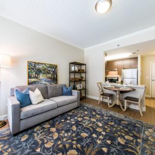 A modern living room with a cozy sofa, decorative rug, and adjacent dining area leading to the kitchen.