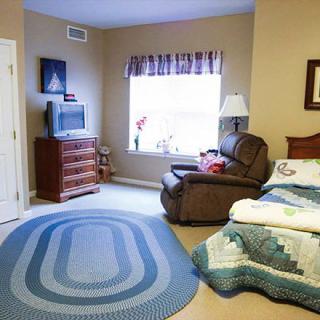 A cozy bedroom with an armchair, bed, dresser, and television arranged around a large oval rug.