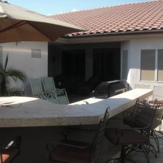 A sunny outdoor patio with a barbecue area and seating under an umbrella.