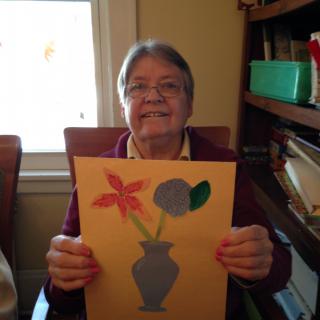 A person holding up a paper artwork of flowers in a vase.