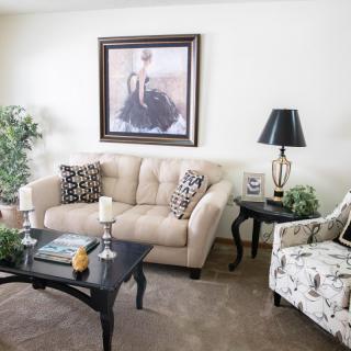 A cozy living room with a beige sofa, patterned armchair, and stylish coffee table, adorned with elegant decor and artwork.