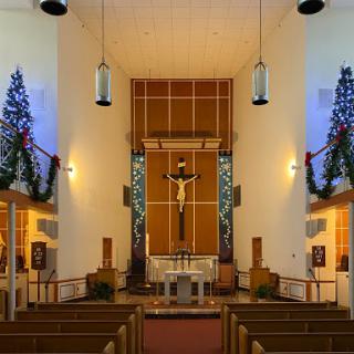 A beautifully decorated church interior, showcasing a central altar with a cross and festive Christmas decorations.