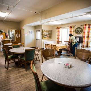 A cozy dining room with tables and chairs, where people are tidying up.