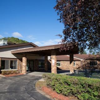 A scenic view of a modern building with stone accents, surrounded by greenery and under a clear blue sky.