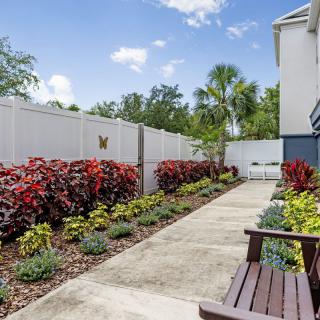 A well-maintained garden with a concrete pathway, colorful flowers, and shrubs alongside a white fence.