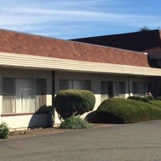 A single-story motel building with neatly trimmed bushes under a blue sky.