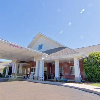 A sunny day view of a building entrance with columns and a covered driveway.